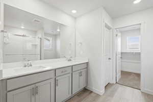 Bathroom featuring light wood-style floors, a shower stall, double vanity, recessed lighting, and a spacious closet
