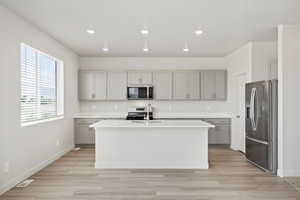 Kitchen featuring appliances with stainless steel finishes, recessed lighting, an island with sink, light wood-style floors, and gray cabinets