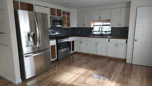 Kitchen featuring stainless steel appliances, dark countertops, wood finished floors, and white cabinets