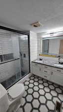 Full bath featuring a textured ceiling, a stall shower, double vanity, and tile patterned floors