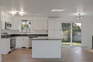 Kitchen with a chandelier, appliances with stainless steel finishes, white cabinetry, a kitchen island, and light wood-style flooring