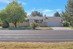 Ranch-style home featuring an attached garage, driveway, brick siding, and a chimney