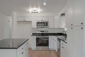 Kitchen with dark countertops, appliances with stainless steel finishes, a textured ceiling, light wood-style floors, and white cabinetry