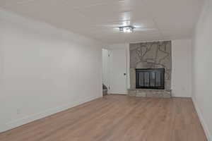 Unfurnished living room featuring a fireplace, light wood finished floors, a drop ceiling, and stairs