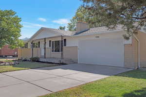 Ranch-style home with driveway, covered porch, a garage, a front yard, and a chimney