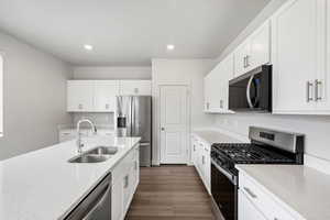 Kitchen featuring appliances with stainless steel finishes, dark wood finished floors, light stone countertops, white cabinets, and recessed lighting