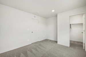 Unfurnished bedroom with a walk in closet, light colored carpet, and recessed lighting