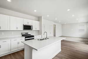 Kitchen with appliances with stainless steel finishes, light stone countertops, white cabinets, recessed lighting, and a center island with sink