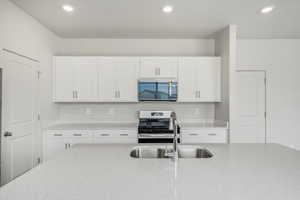Kitchen with white cabinets, stainless steel appliances, light stone counters, and recessed lighting