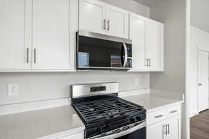 Kitchen with appliances with stainless steel finishes, light stone counters, and white cabinetry