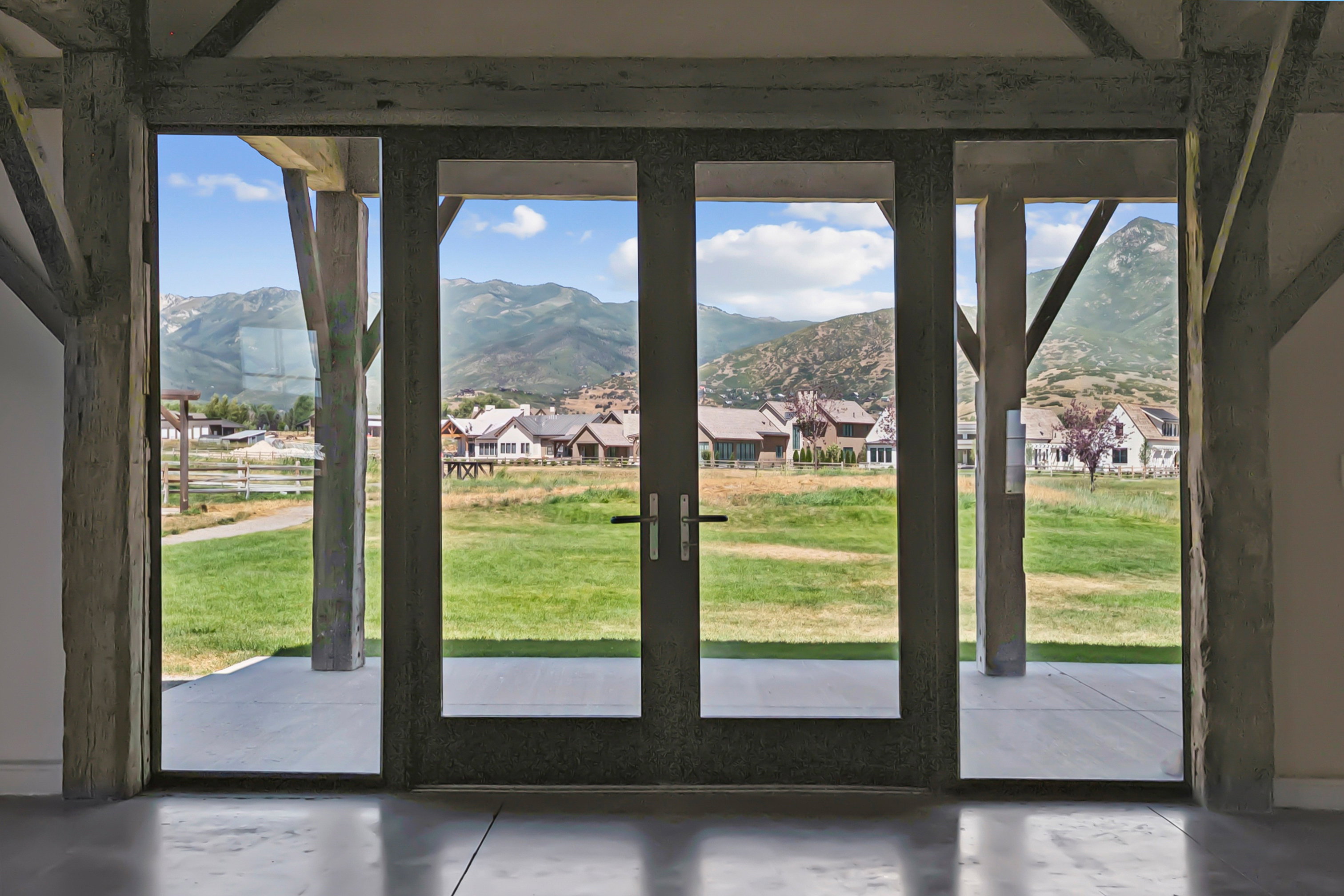 Expansive glass doors opening to a concrete patio, framed by rustic timber beams and posts