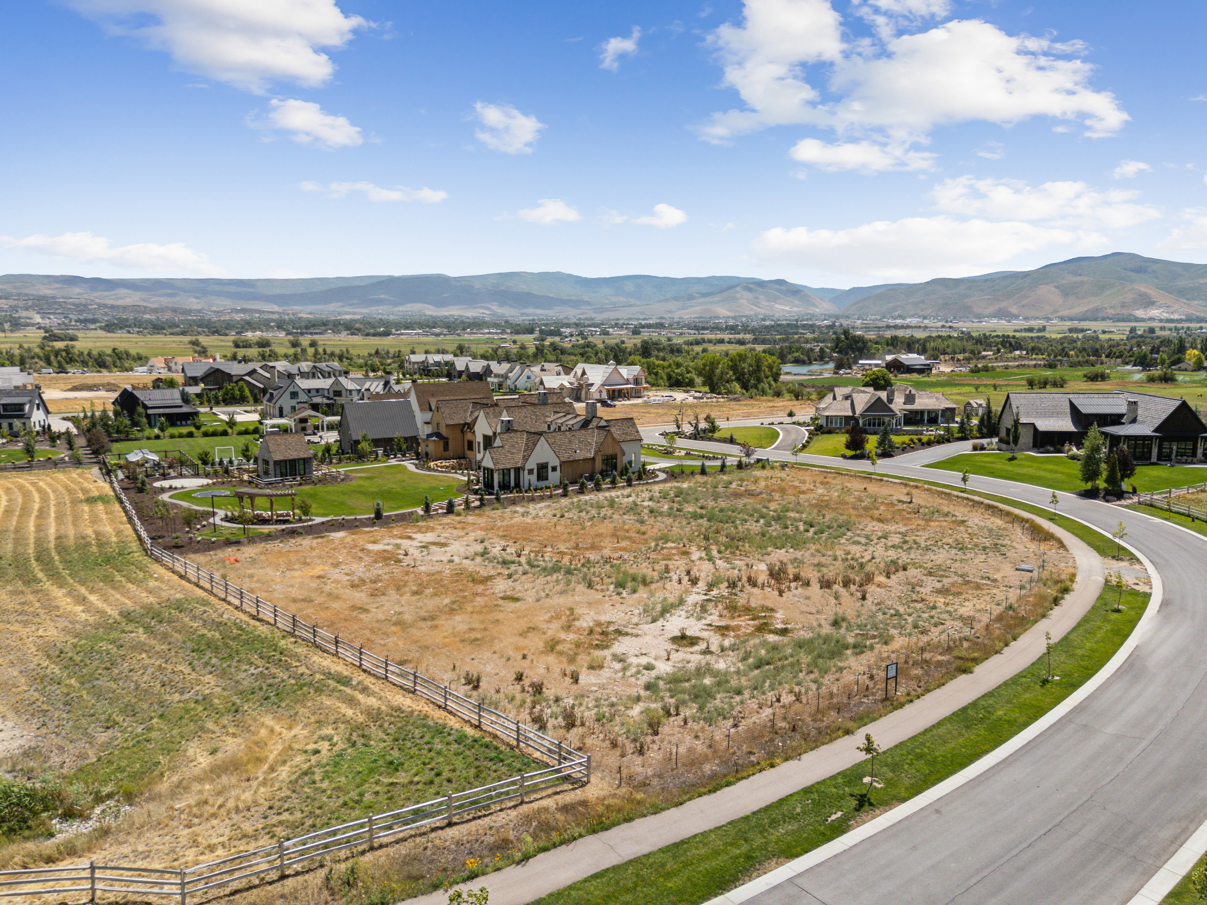 Expansive parcel featuring a curved paved roadway, established curbing, and a surrounding split-rail fence