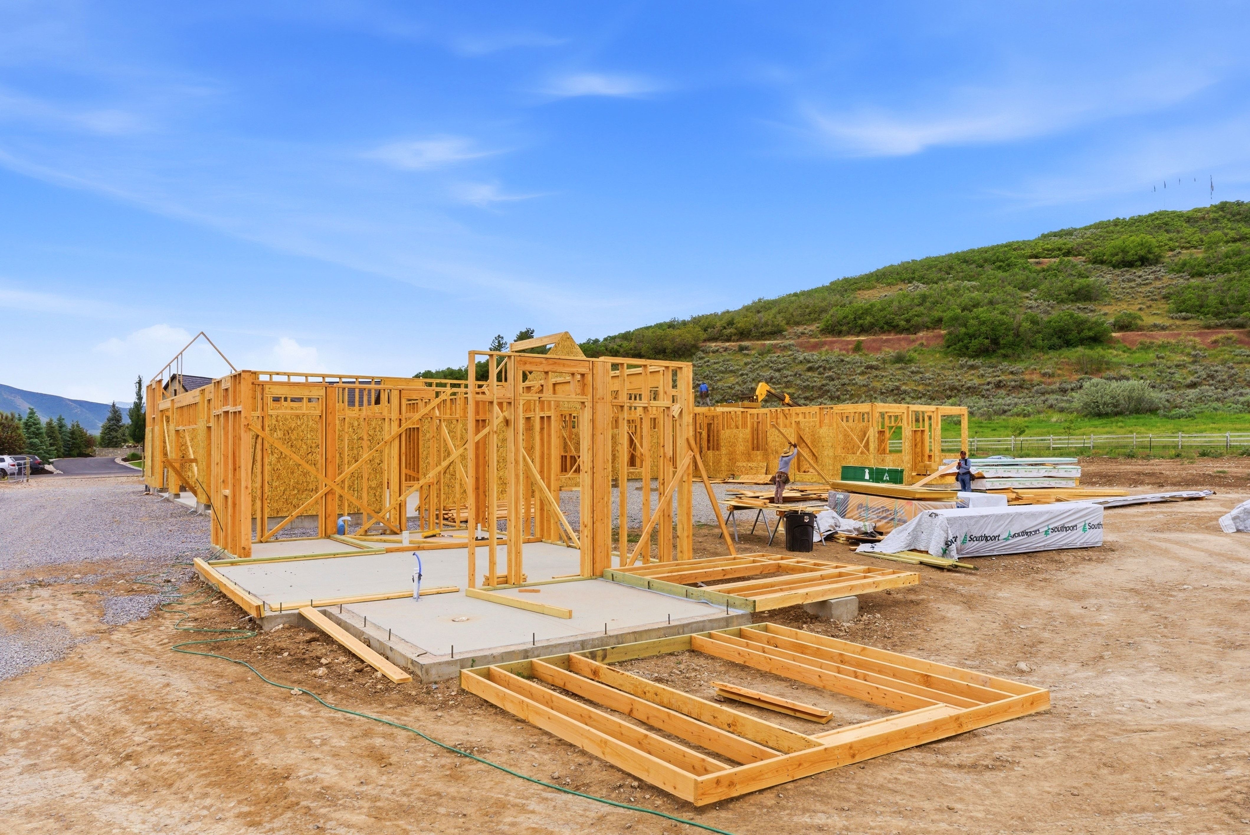 New construction framing with a concrete foundation, surrounded by a natural hillside and distant mountains