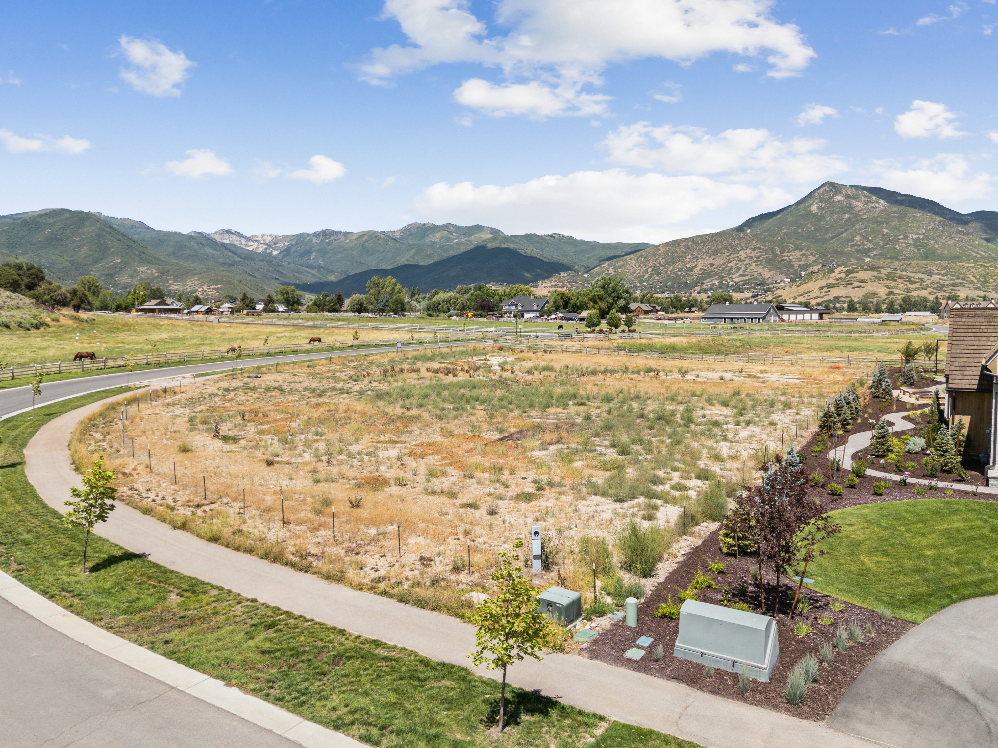 Expansive undeveloped parcel featuring a paved pathway, a landscaped perimeter, and direct access to a paved road