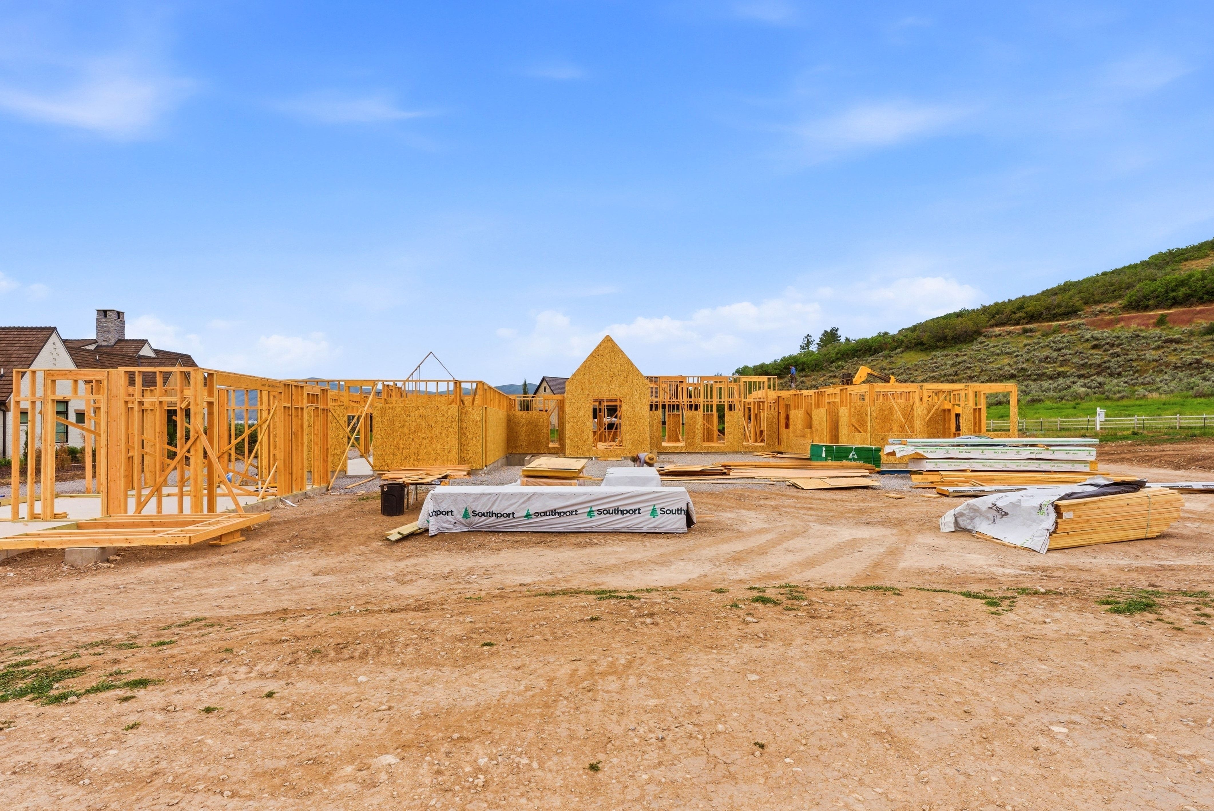 New construction framing with lumber and building materials on-site, set against a natural hillside