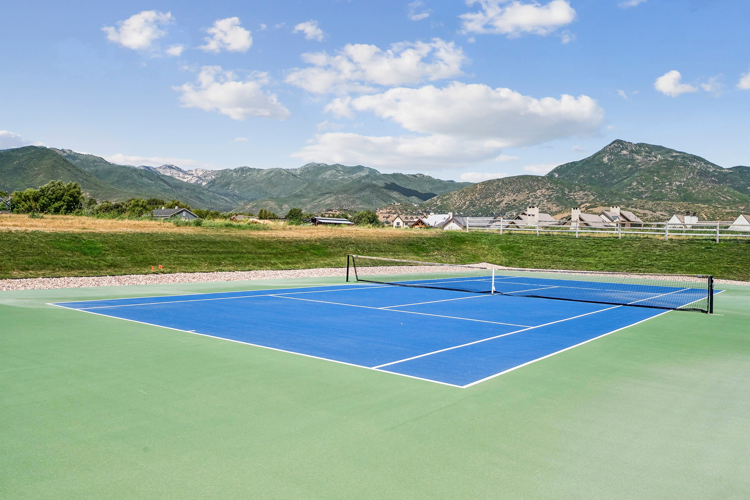 Full-size tennis court featuring a blue playing surface and green surrounding area