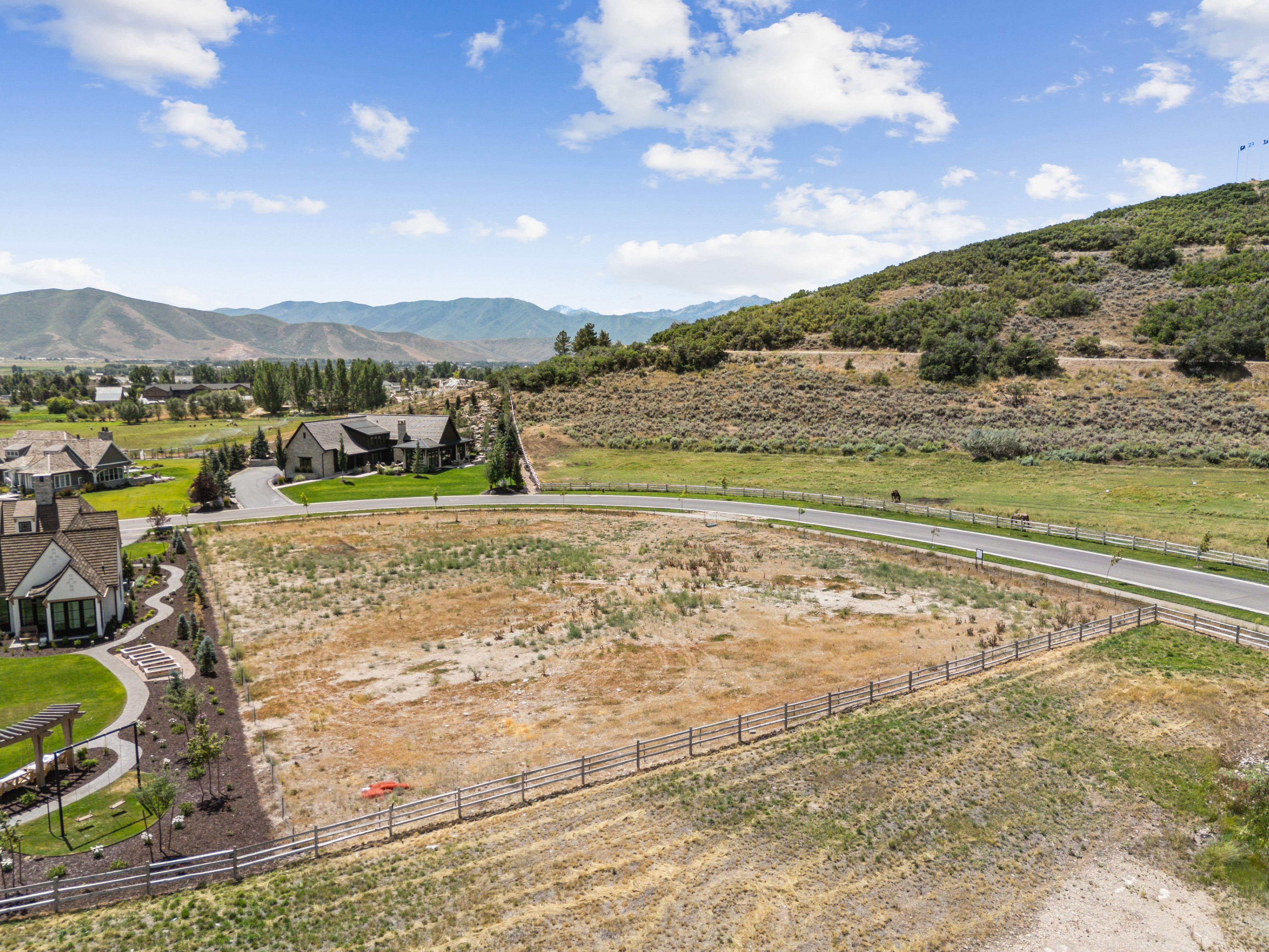 Expansive undeveloped lot featuring a wooden perimeter fence, bordering a paved road and a natural hillside