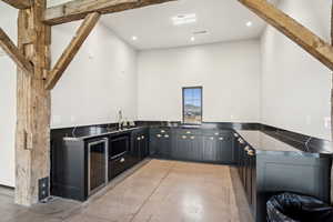Kitchen with finished concrete flooring, dark cabinetry, dark countertops, wine cooler, and recessed lighting