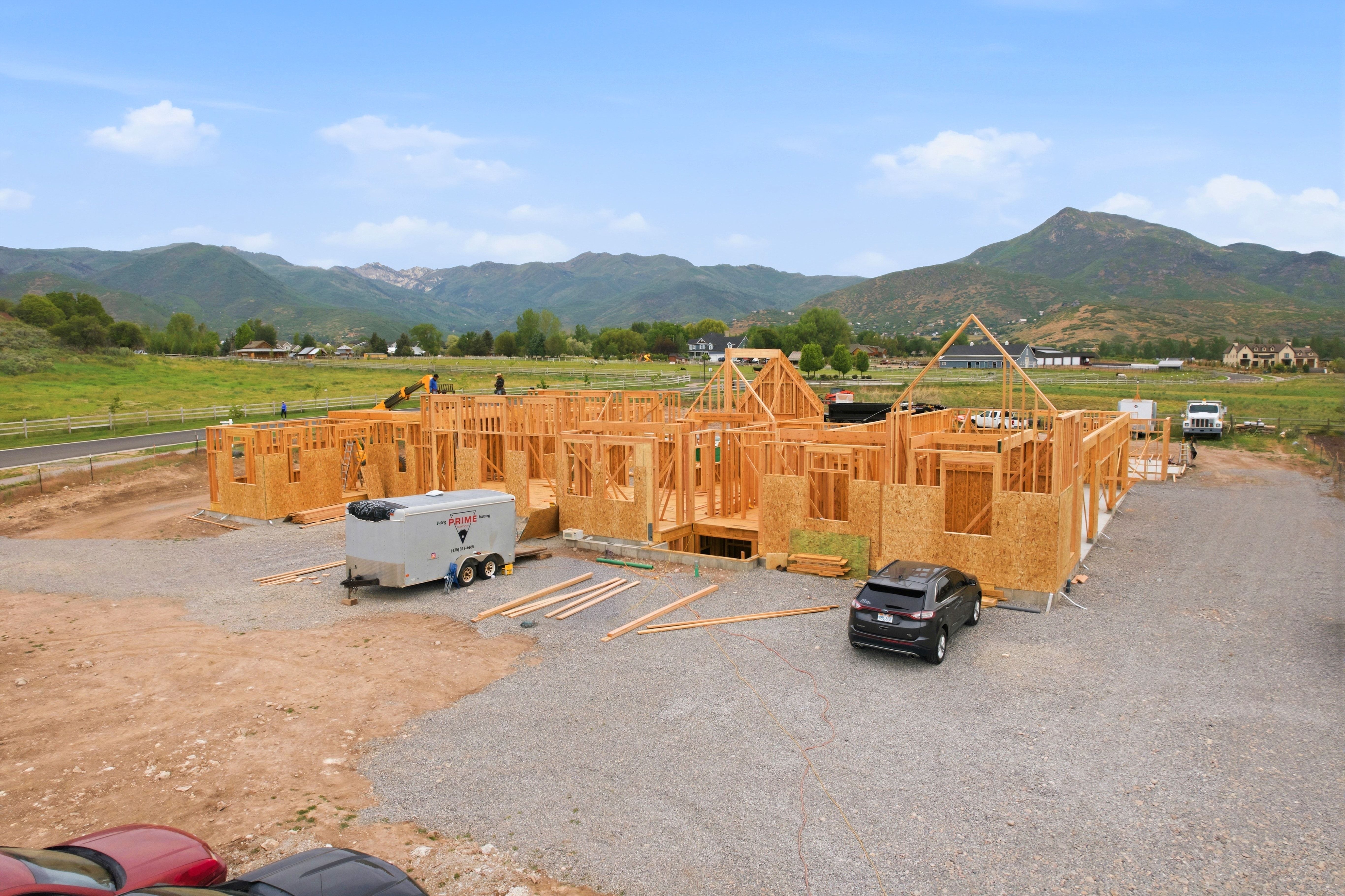 New construction framing featuring multiple gables and dormers, situated on a large lot with natural landscaping