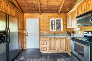 Kitchen with appliances with stainless steel finishes, wood walls, wooden ceiling, stone tile flooring, and light stone counters