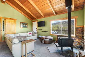 Carpeted living area with a wood stove, a wooden ceiling with exposed beams, and high vaulted ceiling