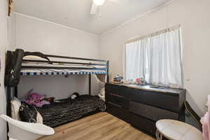 Bedroom with wood finished floors, crown molding, and ceiling fan