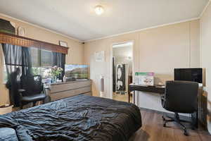Bedroom featuring wood finished floors, ornamental molding, and an office area