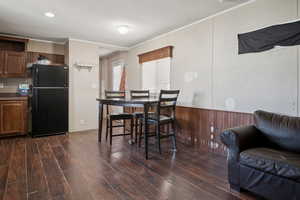 Dining space with dark wood-style floors, crown molding, wood walls, and a wainscoted wall