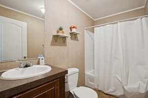 Full bathroom with ornamental molding, vanity, shower / bathtub combination with curtain, and wallpapered walls
