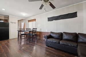 Living room with ornamental molding, wood finished floors, a ceiling fan, wooden walls, and a wainscoted wall