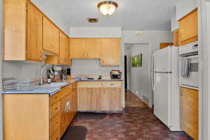 Kitchen with white appliances, light countertops, a textured ceiling, and brick patterned floors