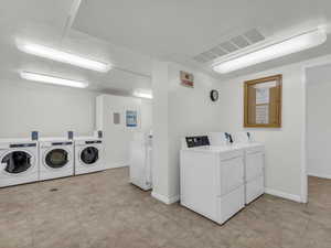 Communal laundry room with independent washer and dryer and light tile patterned floors