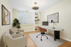 Office area featuring wood finished floors and built in shelves, virtually staged.