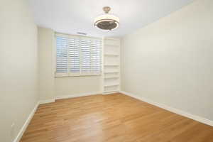 Unfurnished room with built in shelves and wood finished floors, virtually decluttered.