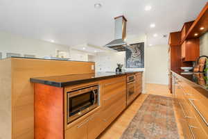 Kitchen featuring light wood-type flooring, dark countertops, island range hood, stainless steel appliances, and recessed lighting