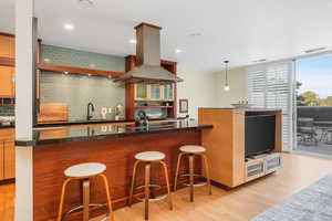 Kitchen with backsplash, island range hood, light wood-type flooring, a breakfast bar, and recessed lighting