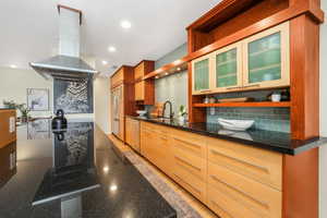 Kitchen with decorative backsplash, island exhaust hood, open shelves, dark stone counters, and recessed lighting
