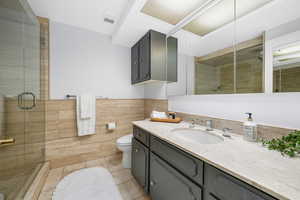 Bathroom featuring vanity, tile patterned floors, tile walls, a shower stall, and a wainscoted wall