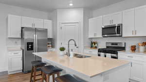 Kitchen with appliances with stainless steel finishes, wood finished floors, white cabinets, and an island with sink