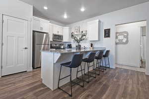 Kitchen featuring stainless steel appliances, stone countertops, a kitchen bar, a peninsula, and white cabinetry