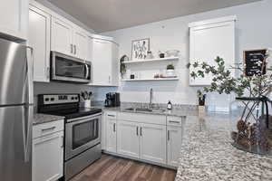Kitchen featuring stainless steel appliances, dark wood-style flooring, white cabinetry, light stone counters, and open shelves