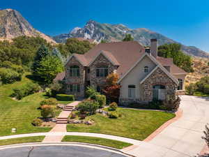 View of front of house featuring stone siding, a chimney, a mountain view, a front lawn, and roof with shingles