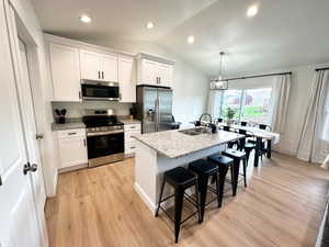 Kitchen with appliances with stainless steel finishes, light wood-type flooring, a breakfast bar, white cabinetry, and lofted ceiling