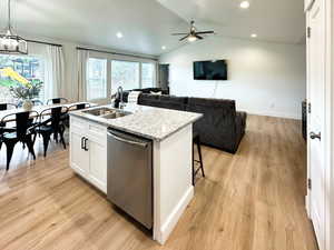 Kitchen featuring lofted ceiling, dishwasher, a center island with sink, white cabinets, and light stone countertops