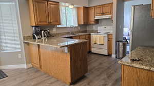 Kitchen featuring white range with electric stovetop, freestanding refrigerator, light wood-style floors, a peninsula, and light stone counters