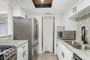 Kitchen featuring light wood-type flooring, stainless steel appliances, decorative backsplash, and white cabinetry