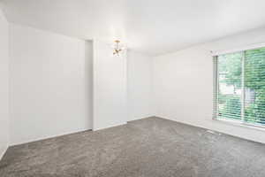 Carpeted spare room featuring a chandelier and baseboards
