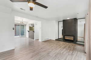 Unfurnished living room featuring light wood-style floors, a large fireplace, ceiling fan, and a chandelier