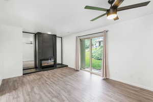 Empty room with a ceiling fan, a large fireplace, and wood finished floors