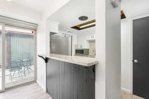 Kitchen with white cabinets, light wood-style floors, stainless steel appliances, and light stone counters